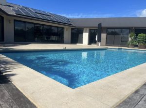 NZ Grinders pool surround non slip bush hammer a swimming pool inset into a deck with concrete strip around edge that has been bush hammered to make non-slip texture